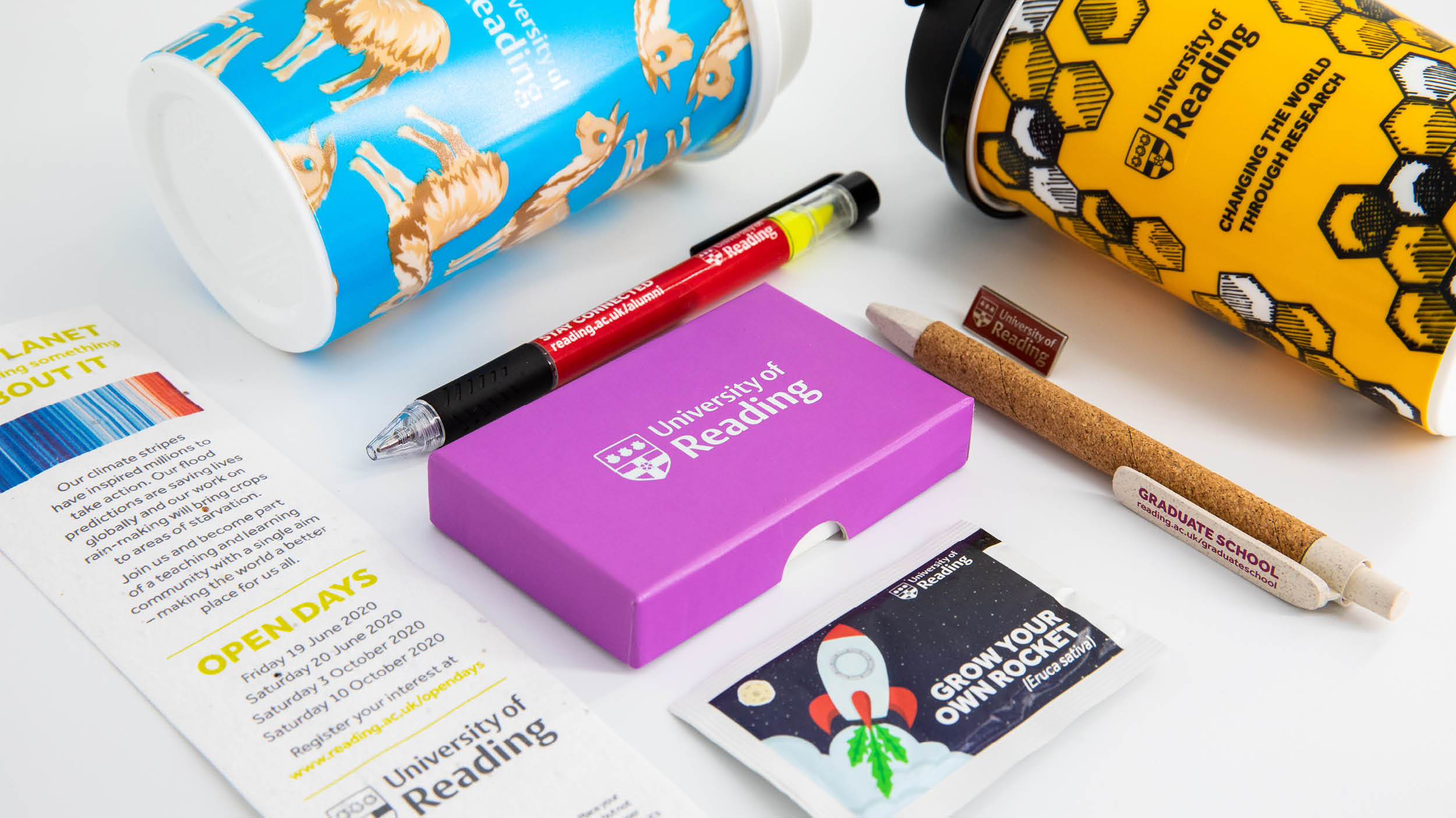 Collection of merchandise items including reusable cups, pens, giveaways and a pin badge