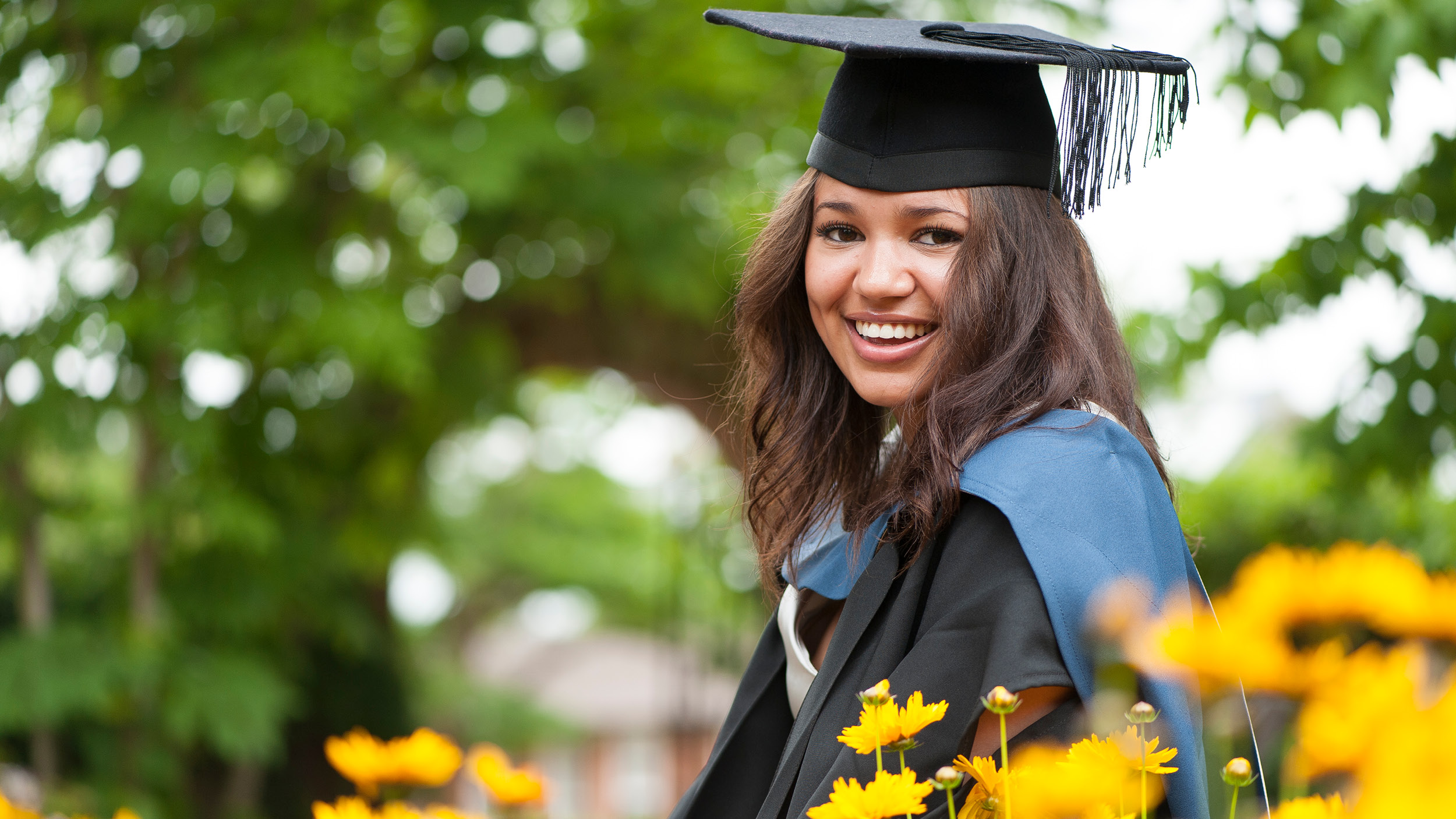 Student in graduation gown and mortar board looks towards the camera