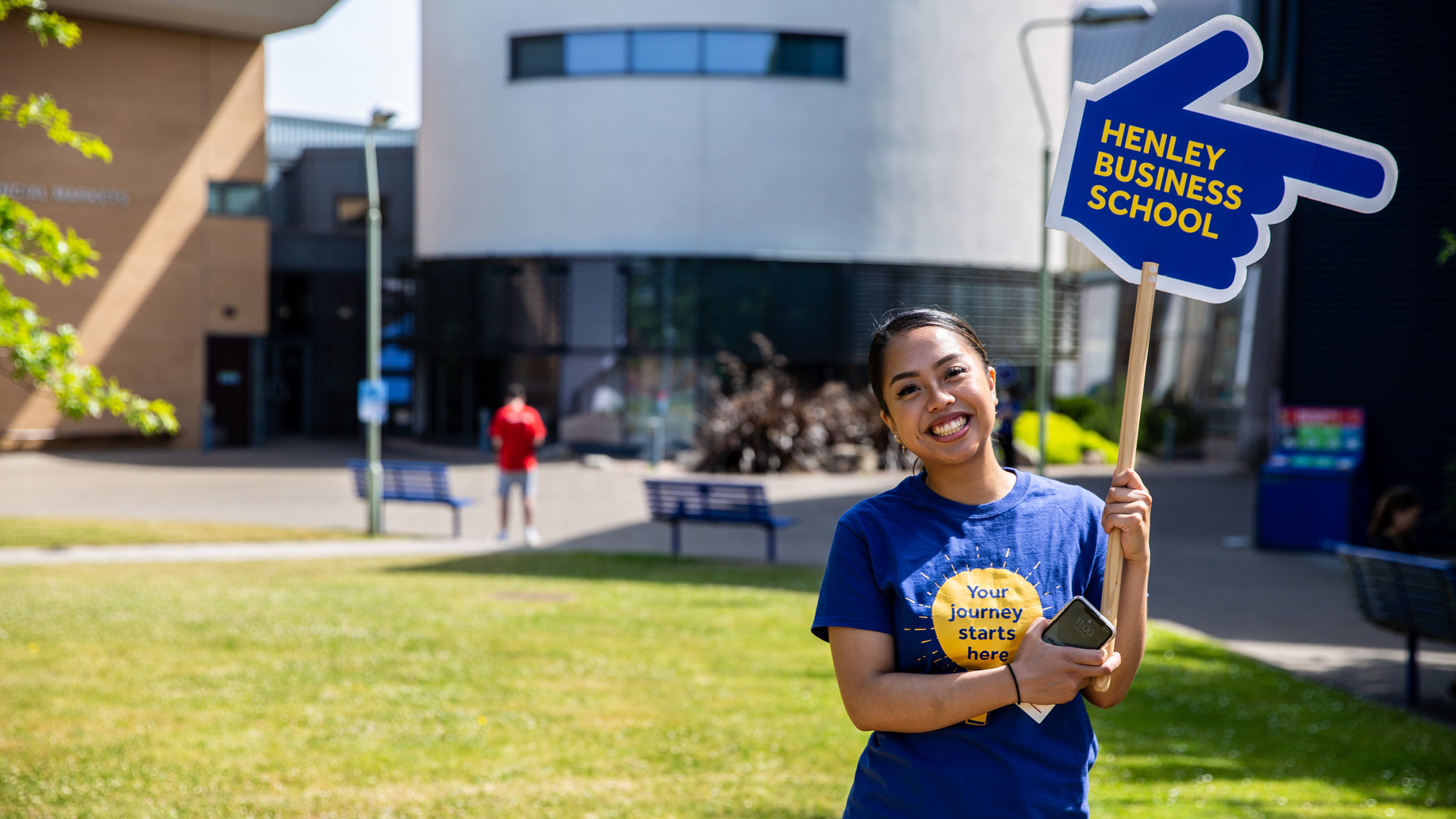 A marshal holds a large hand shaped sign pointing to Henley Business School