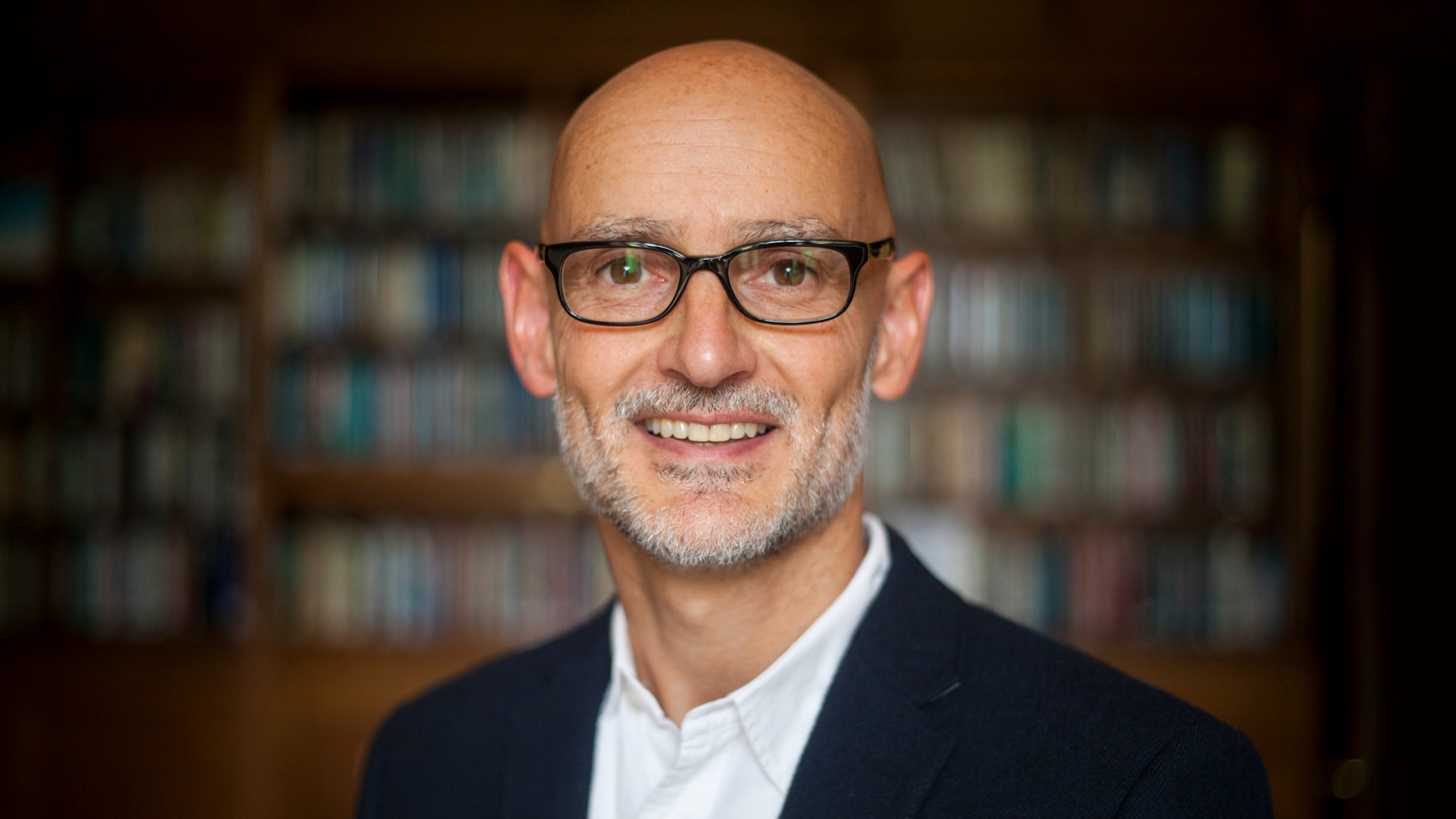 Portrait of a smartly dressed man standing in front of a bookcase