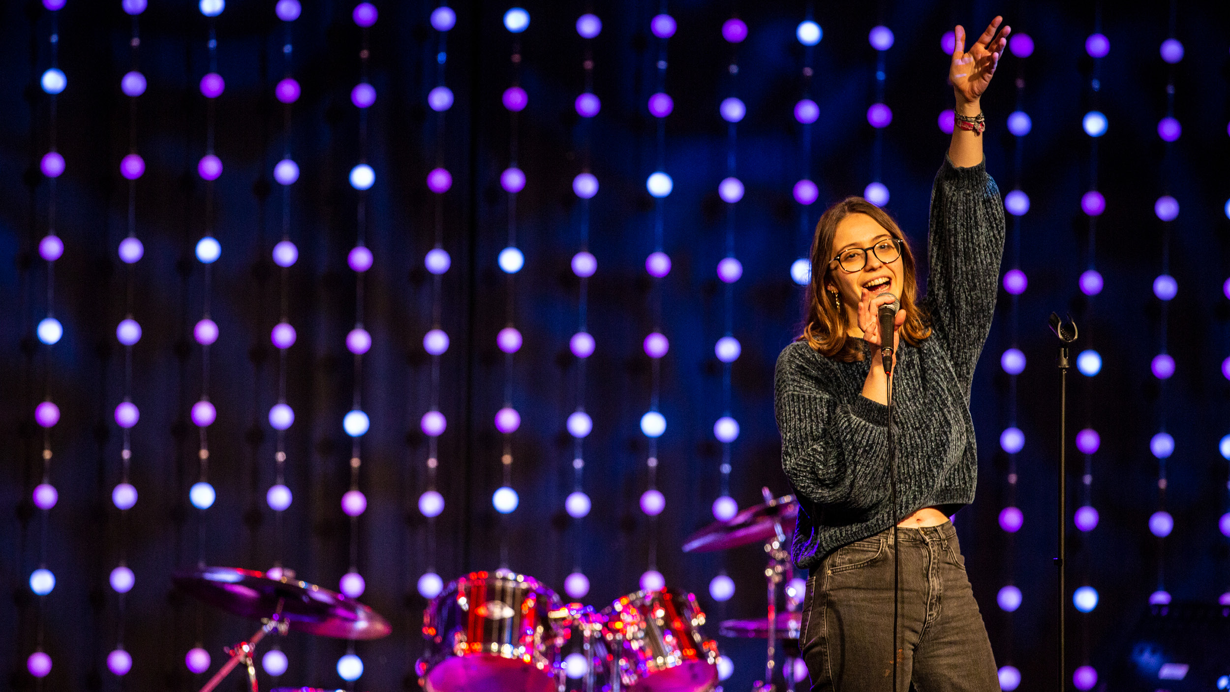 Female student sings in a concert with drums in the background