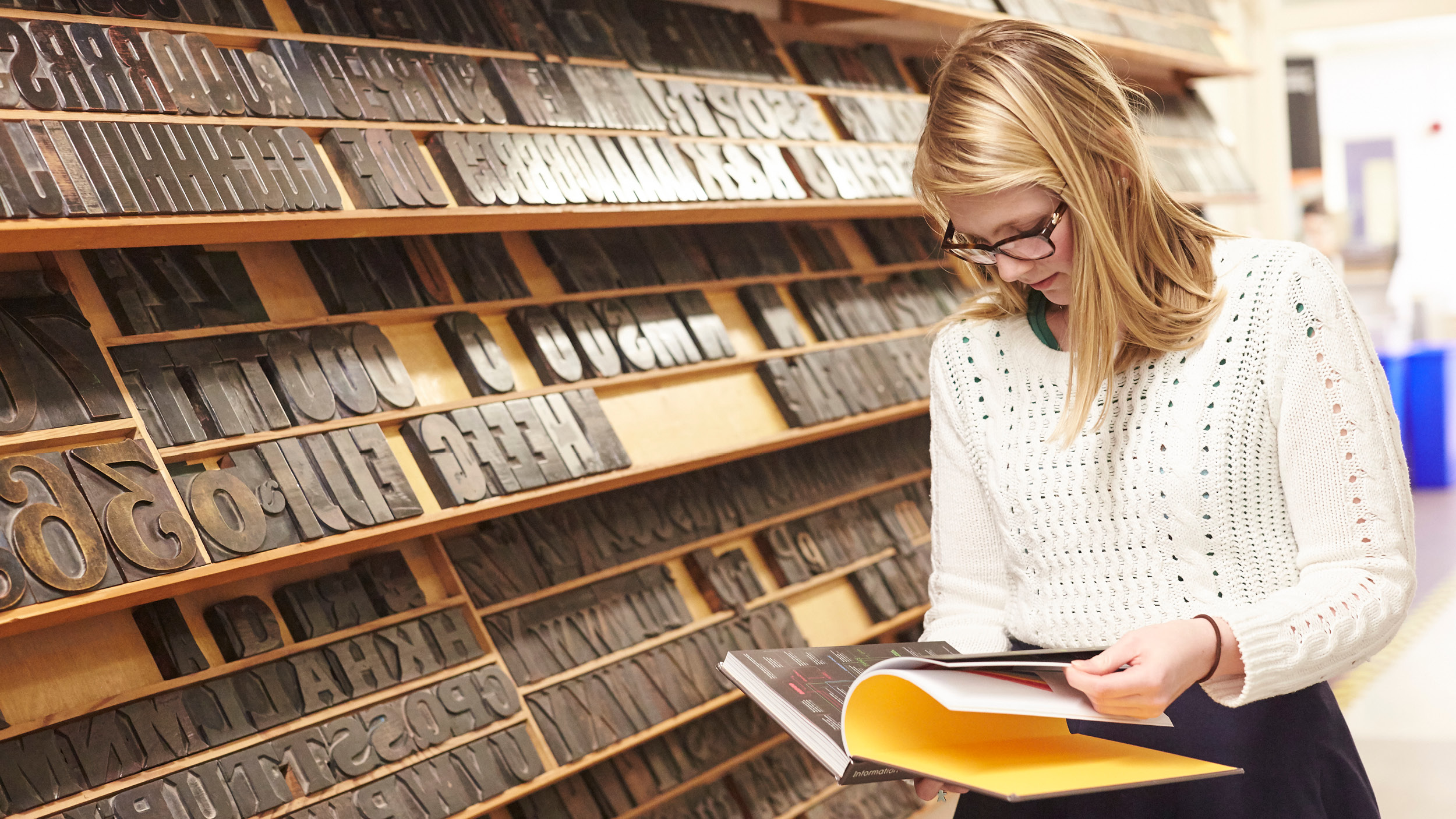 Female student stands next to racks of wooden type in the Typography building