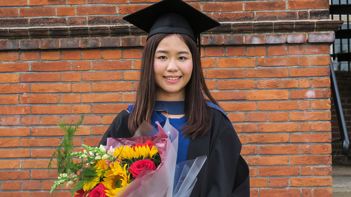 Ada Wong in graduation cap and gown, with a bunch of colorful flowers.