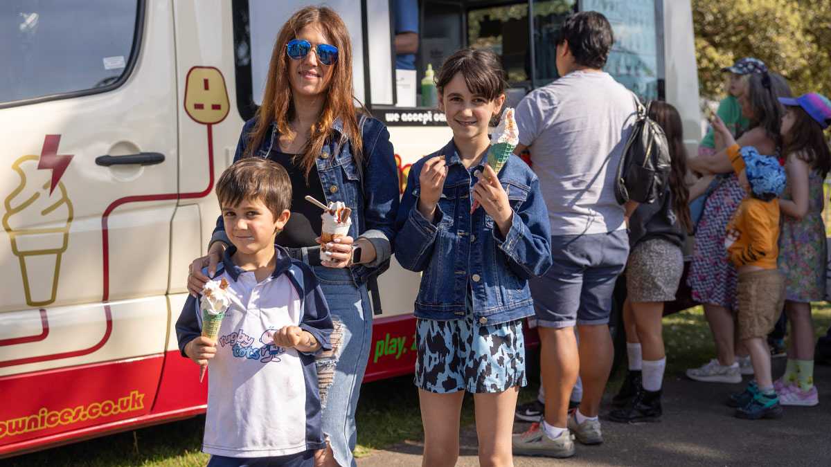 Children and one adult standing in front of an ice cream van, smiling in the sun and eating ice creams.