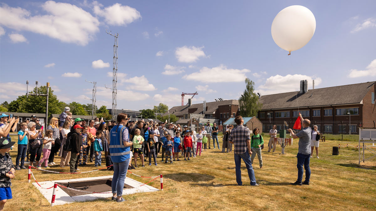 University of Reading's Community Festival 2025, a large group of people are gathered outside the Atmospheric Observatory in the sun,  watching the launch of a weather balloon.