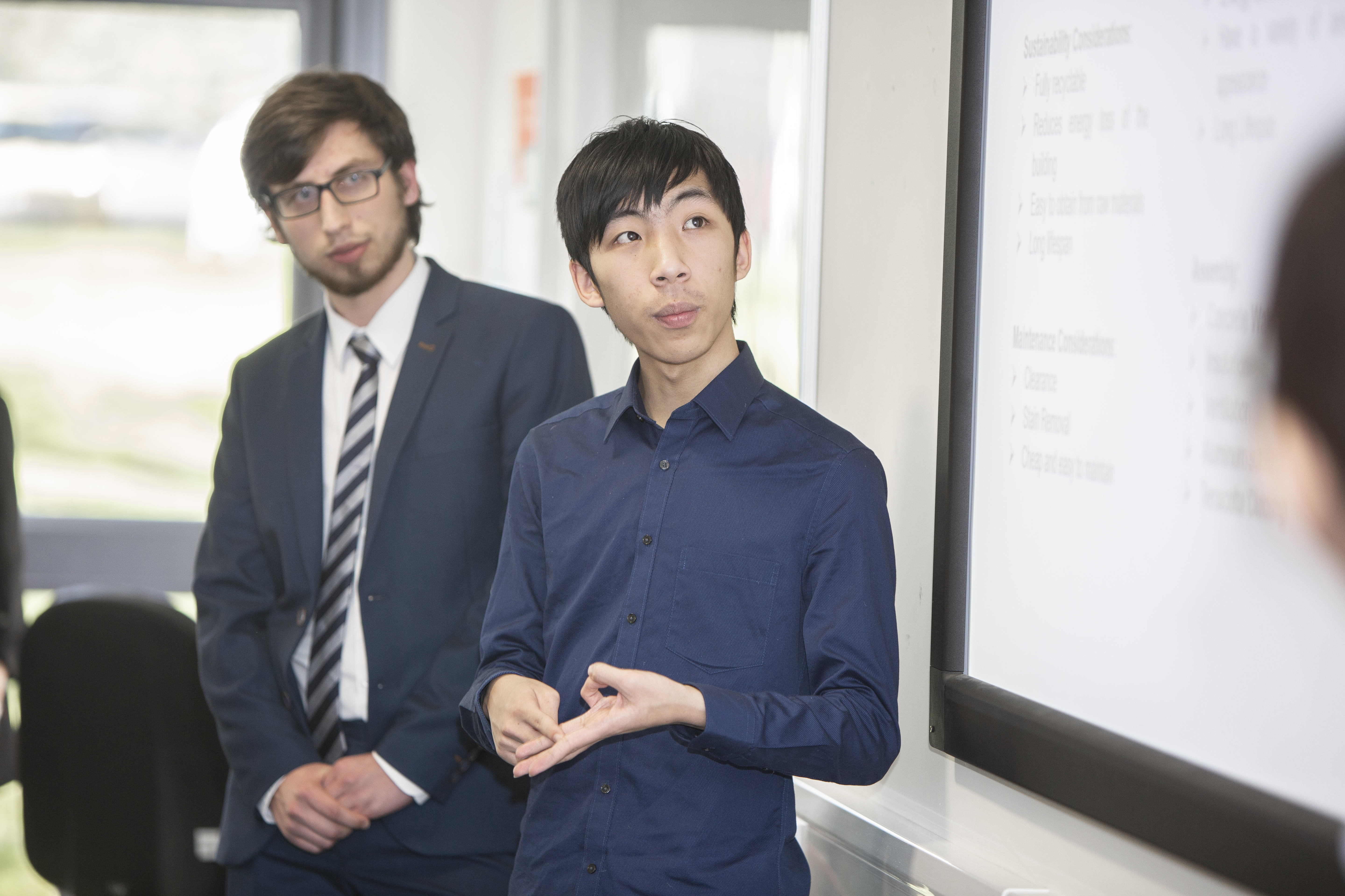 Two men watch an off-camera speaker or presentation.