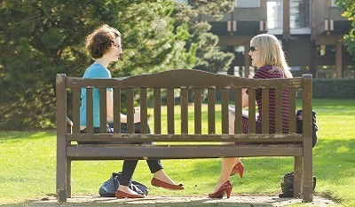 two staff sitting on a bench on campus