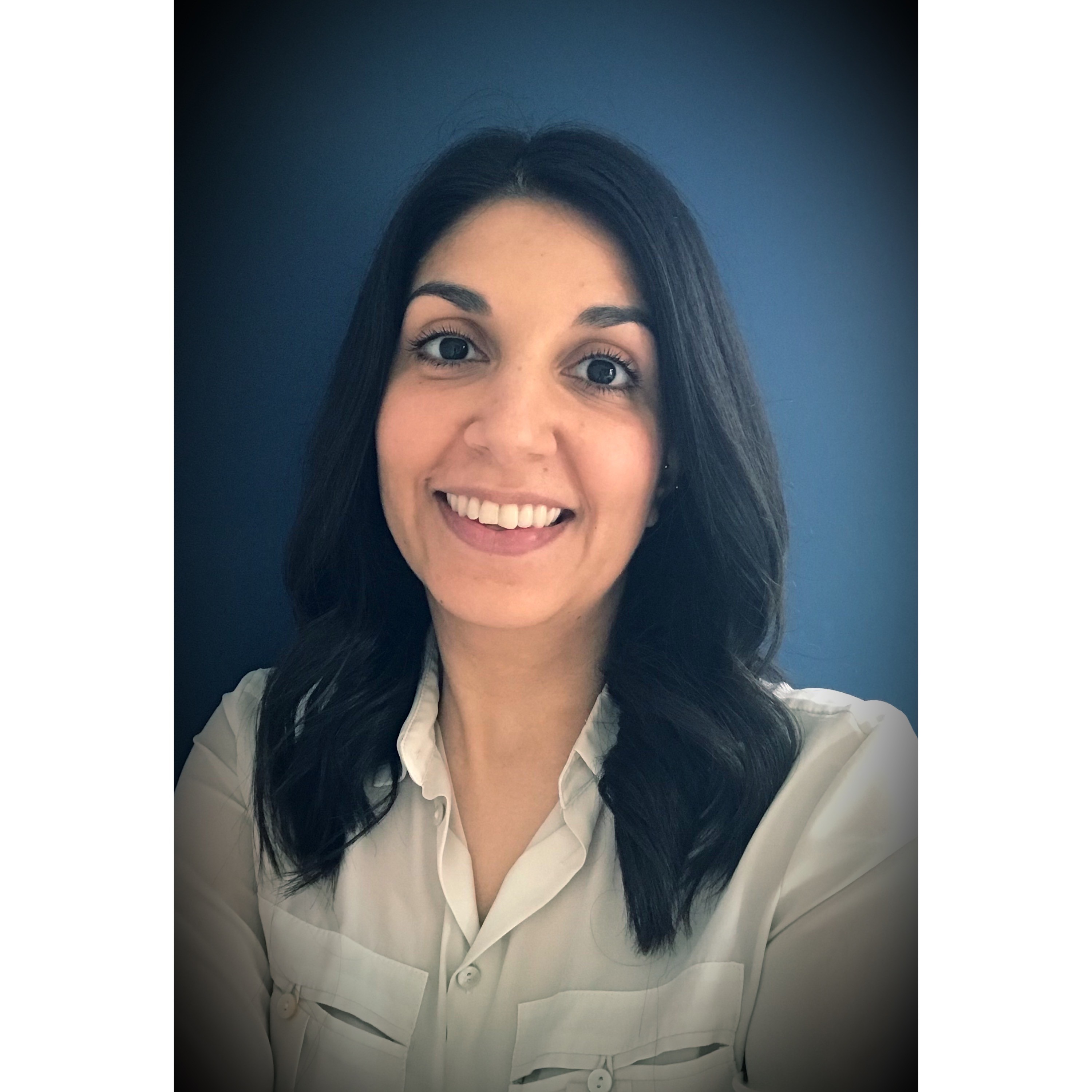 A profile photo of Dr Emma Harris. With dark hair and a beige top against a blue background